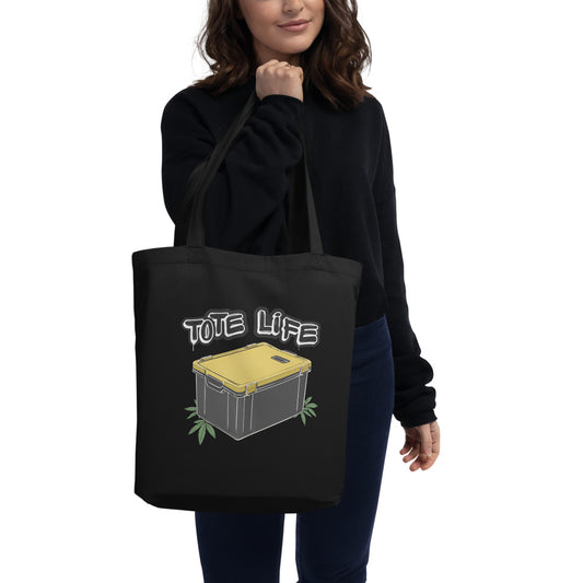 Front view of a woman holding a black eco friendly tote bag with a graphic of a black and yellow plastic tote on the front that reads "Tote Life" 